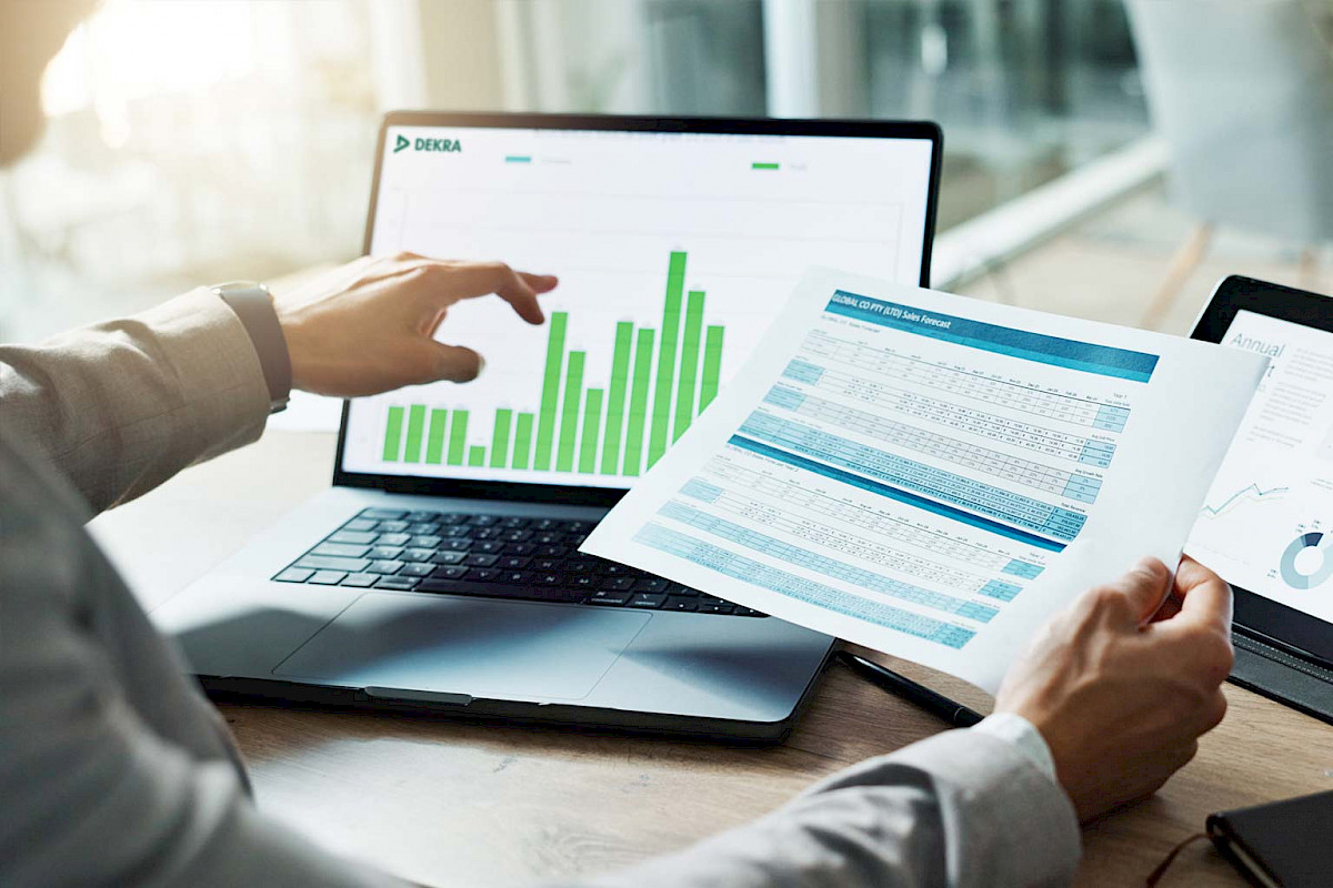 Person analysiert ein Balkendiagramm am Laptop und einen gedruckten Bericht
