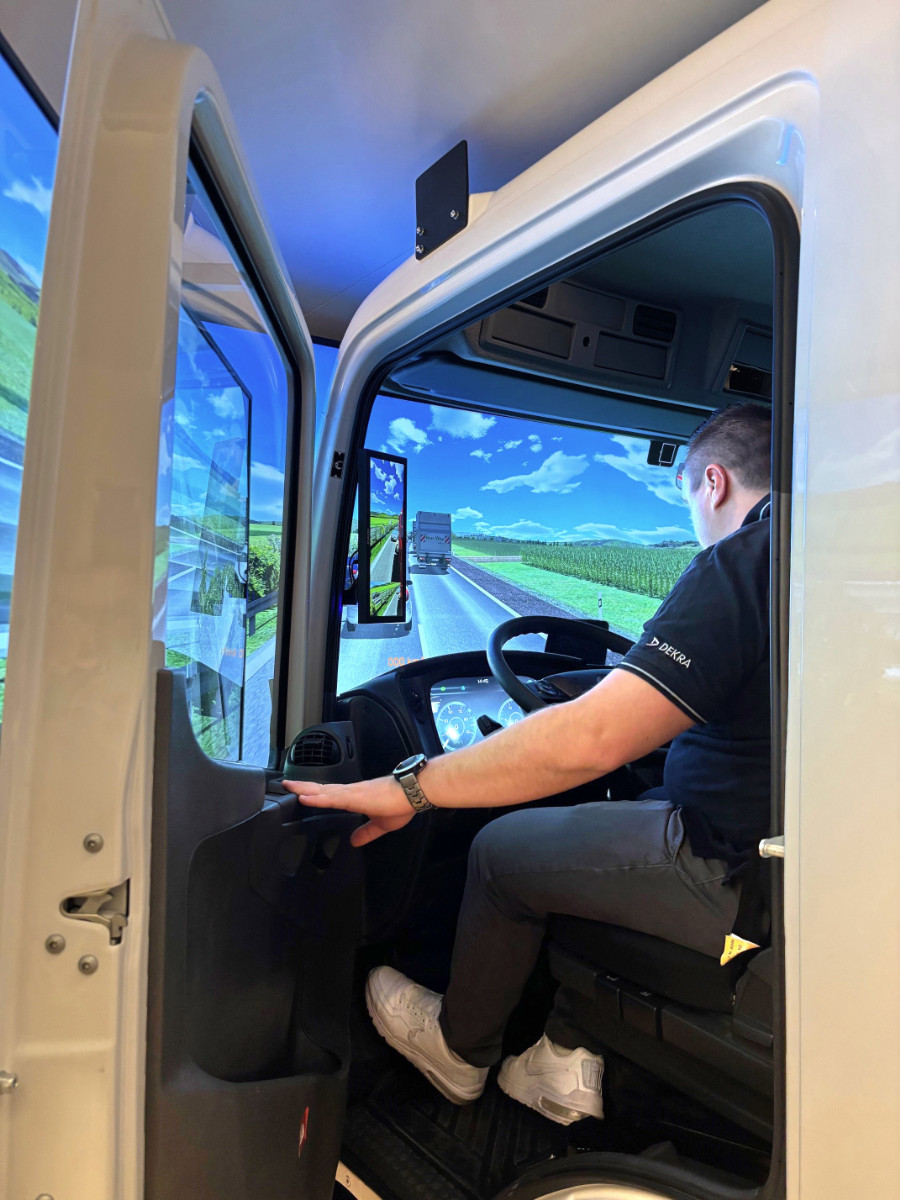Person sitzt in einem DEKRA-Lkw-Fahrsimulator mit Straßenansicht auf den Bildschirmen
